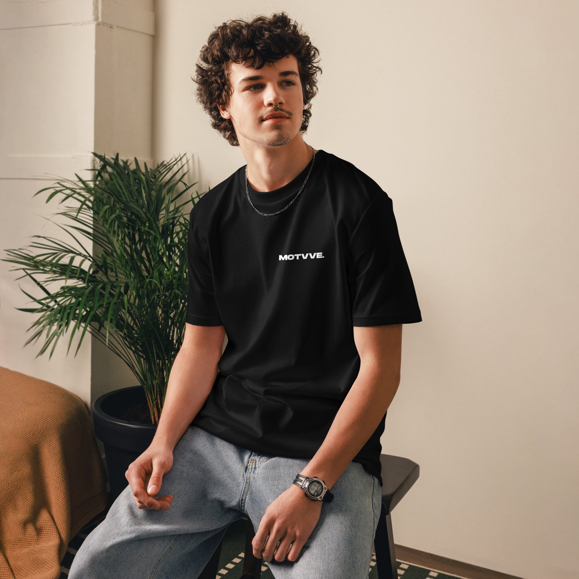 Person wearing a black t-shirt with 'MOTVVE' logo sitting indoors.